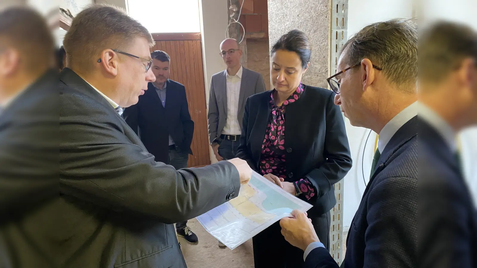 Hohenwepels Ortsvorsteher Daniel Strathaus erklärt Bürgermeister Tobias Scherf (rechts) und Regierungspräsidentin Anna Bölling den Erweiterungsbau anhand der Zeichnungen. (Foto: Stadt Warburg)