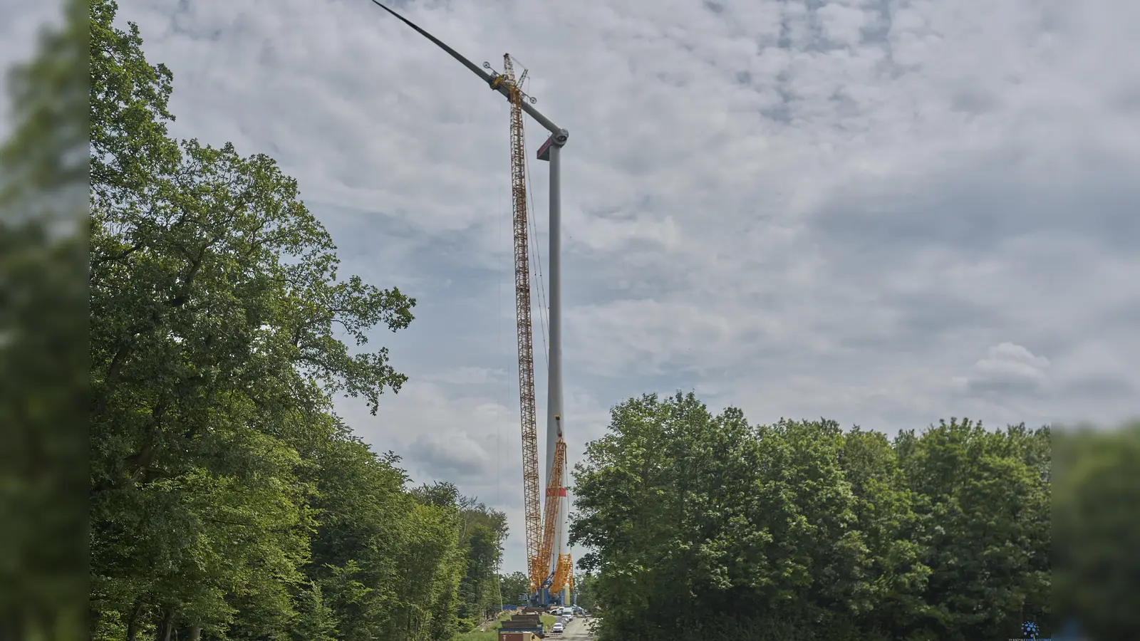 Präzisionsarbeit in schwindelerregender Höhe: Das erste der jeweils rund 25 Tonnen und 78 Meter langen Rotorblätter konnte jetzt an der ersten Anlage auf dem Bratberg montiert werden. Wie riesig die Anlage ist, lässt sich im Vergleich der am Fuße abgestellten Fahrzeuge erkennen. (Foto: Stefan Bönning)