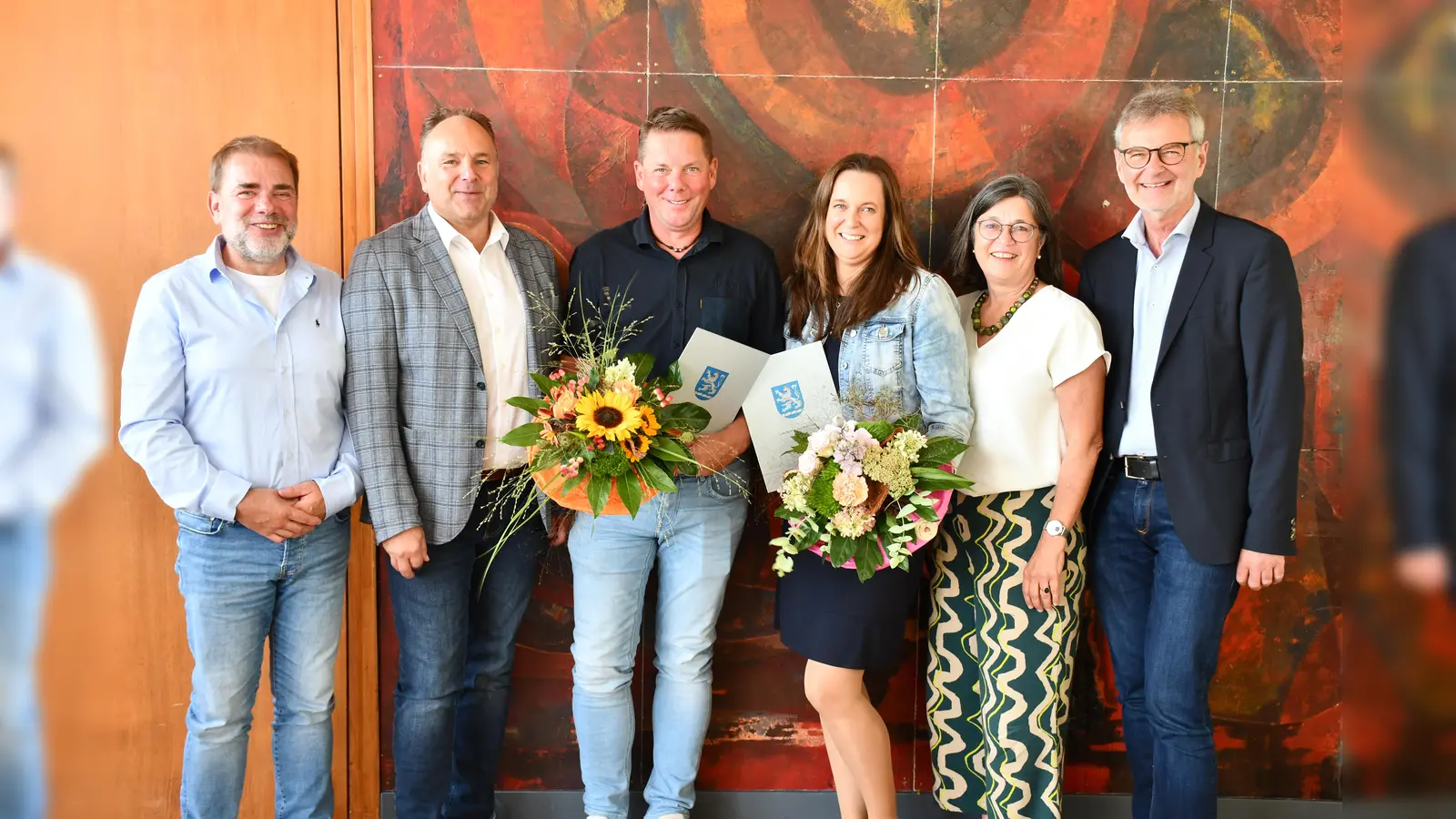 Mit Blumenstrauß und Urkunde während der Jubiläumsfeierlichkeiten bedacht: Sven Henze (r.v.l) und Melanie Hannachi (3.v.r.) zusammen mit ihren Bereichsleitern Ralph Schwekendiek (l.) bzw. Dr. Jutta Klüber-Süßle (2.v.r), Landrat Michael Schünemann (2.v.r.) und dem zuständigen Dezernenten Kreisbaurat Ralf Buberti (r.). (Foto: Peter Drews/Landkreis Holzminden)